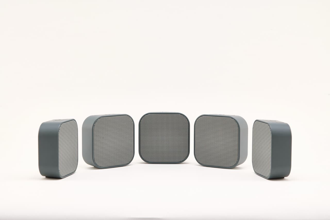 Five slate gray Dio Node speakers arranged in a shallow arc on a white background, mesh grilles facing forward.