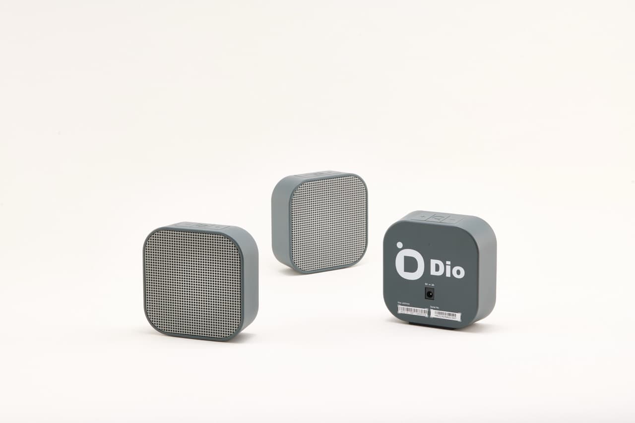 Three Dio Node speakers on a white background, two turned to the mesh grille and one showing the branded back panel.