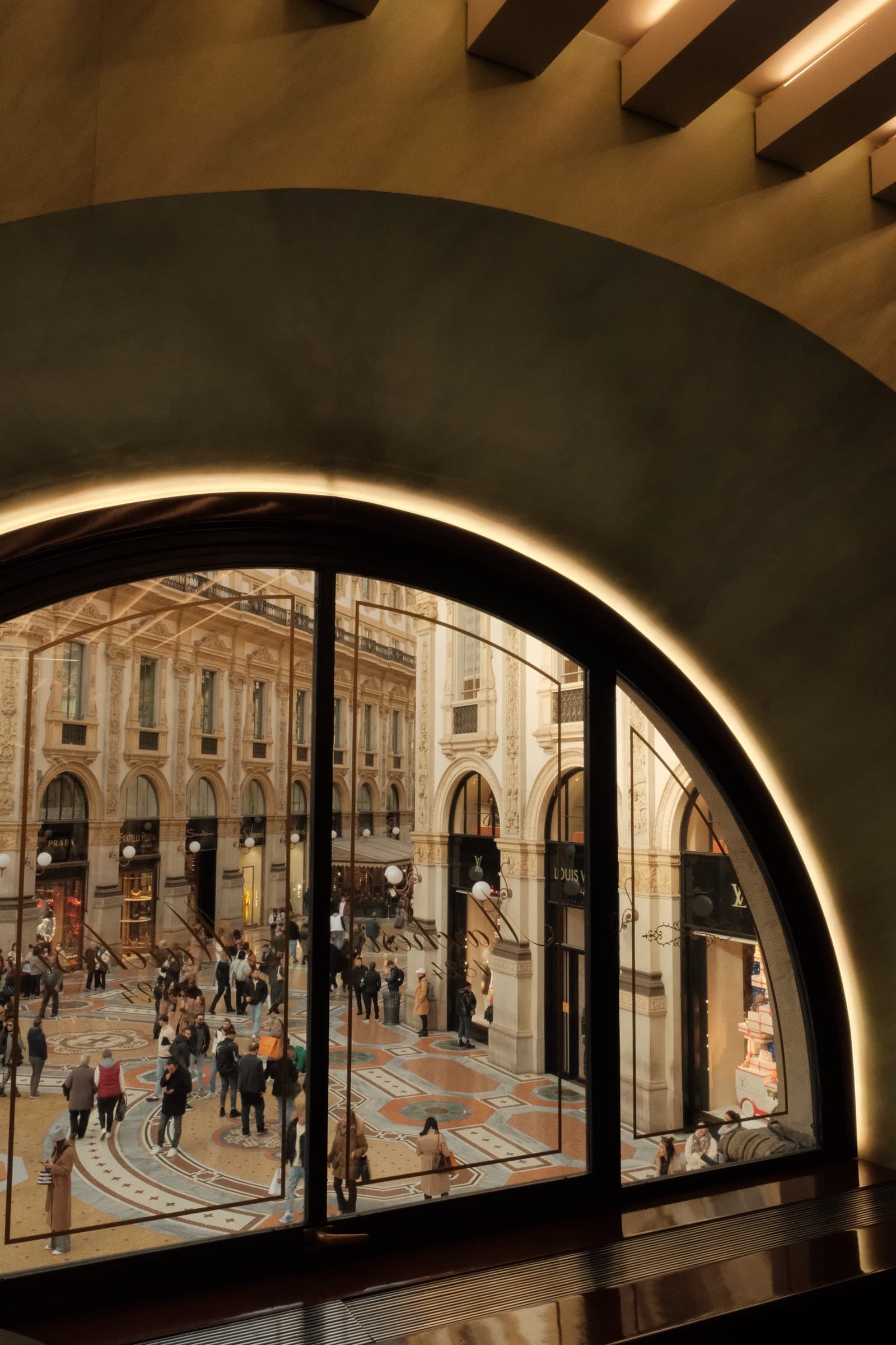 Arched gallery window overlooking the mosaic floor and storefronts of a grand Milanese shopping arcade