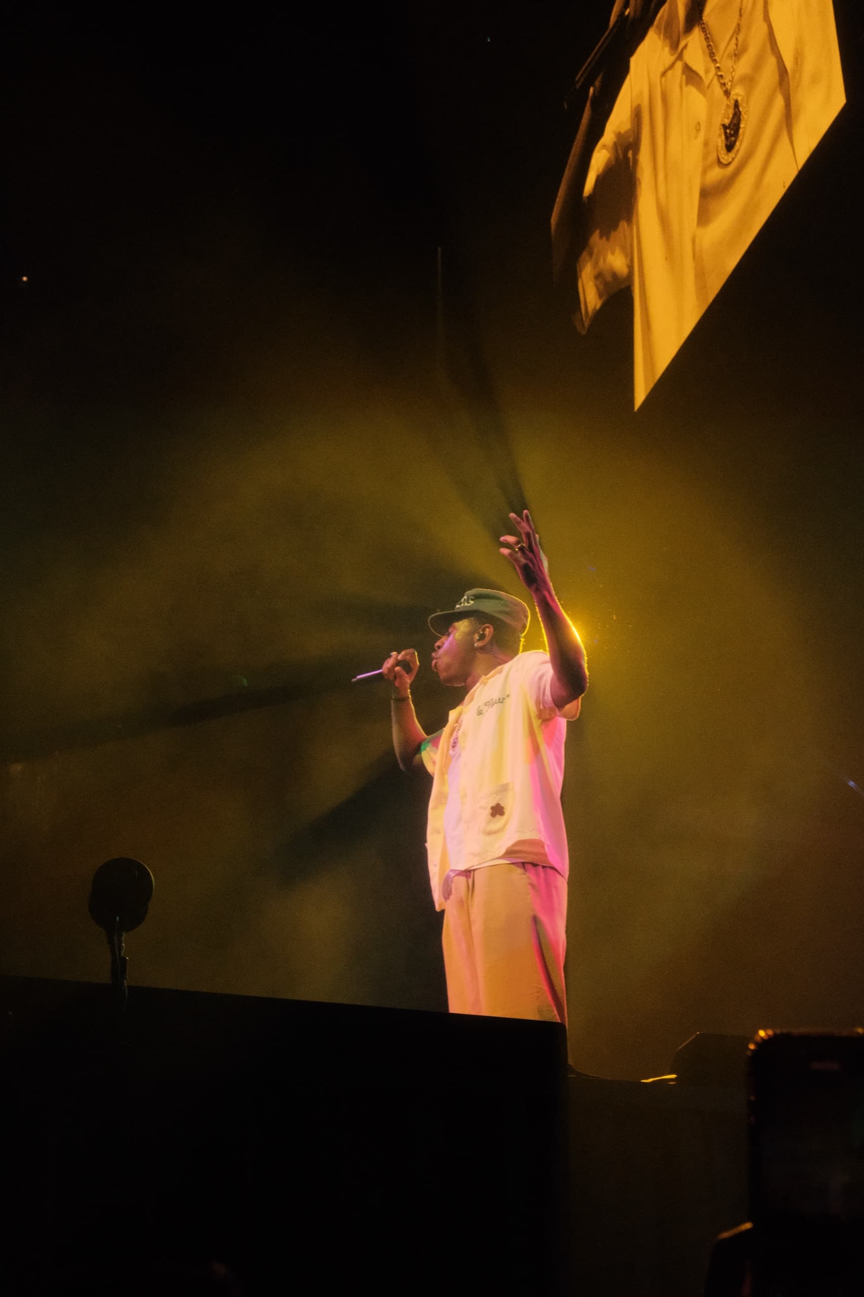 A performer in a pale suit raises one arm under a yellow-green wash, with a banner hanging above the stage.