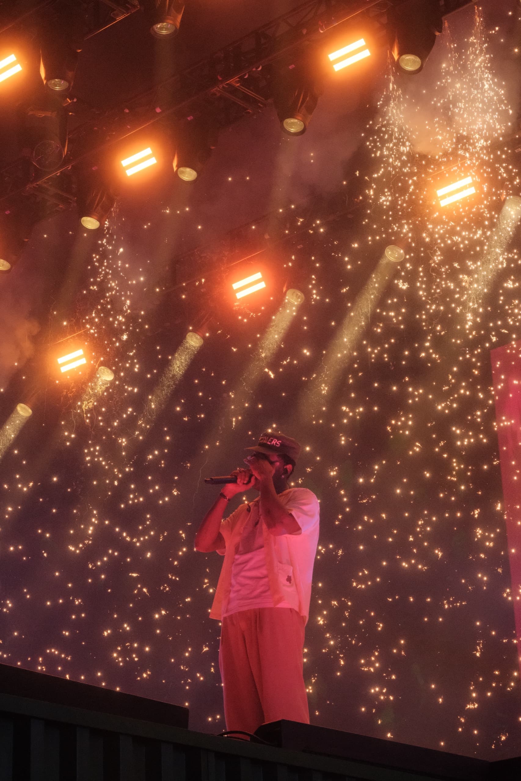 A performer at the mic beneath rows of orange neon bars, sparks falling across the screen behind the stage.