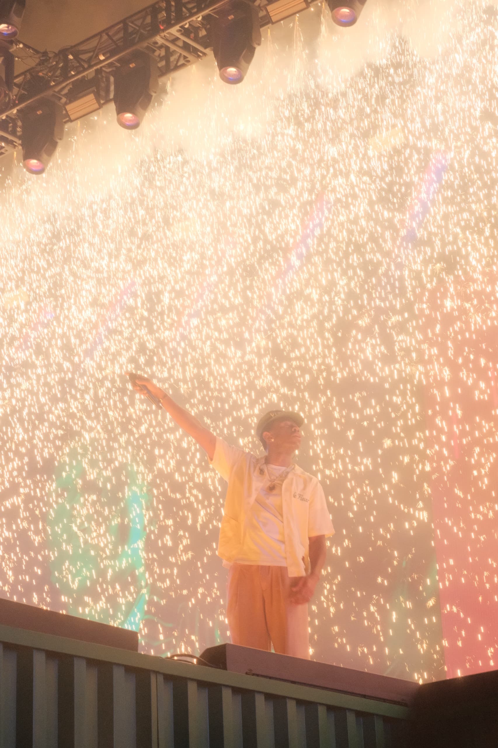 A performer with one arm raised in front of a wall-sized screen filled with white sparks.